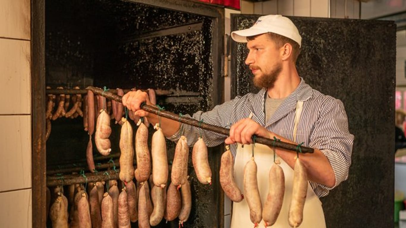 Im Fleischerhandwerk ist Nachwuchs gesucht: Der Auszubildende Maurice Münch hängt Würste zum Räuchern in den Räucherofen.