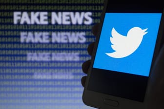 Ein Handy mit Twitter-Symbol, im Hintergrund ein "Fake News"-Schriftzug: Auf Twitter sollen sich Corona-Verschwörungstheorien verbreiten.
