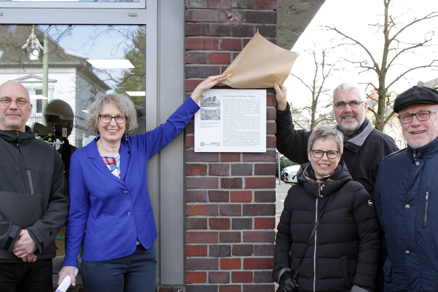 Achim Krüger (städtische Gebäudewirtschaft), Petra Kroll (Ev. Stiftung Volmarstein), Ina Hanemann (Denkmalbehörde), Jens Bergmann (Heimatbund) und Bezirksbürgermeister Dietmar Thieser enthüllen die Infotafel am Alten Stadtbad Haspe.