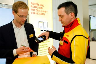 David Krakow (l), Produktmanager bei DHL Post & Paket Deutschland, demonstriert das Frankieren von Paketen mit dem Handy.