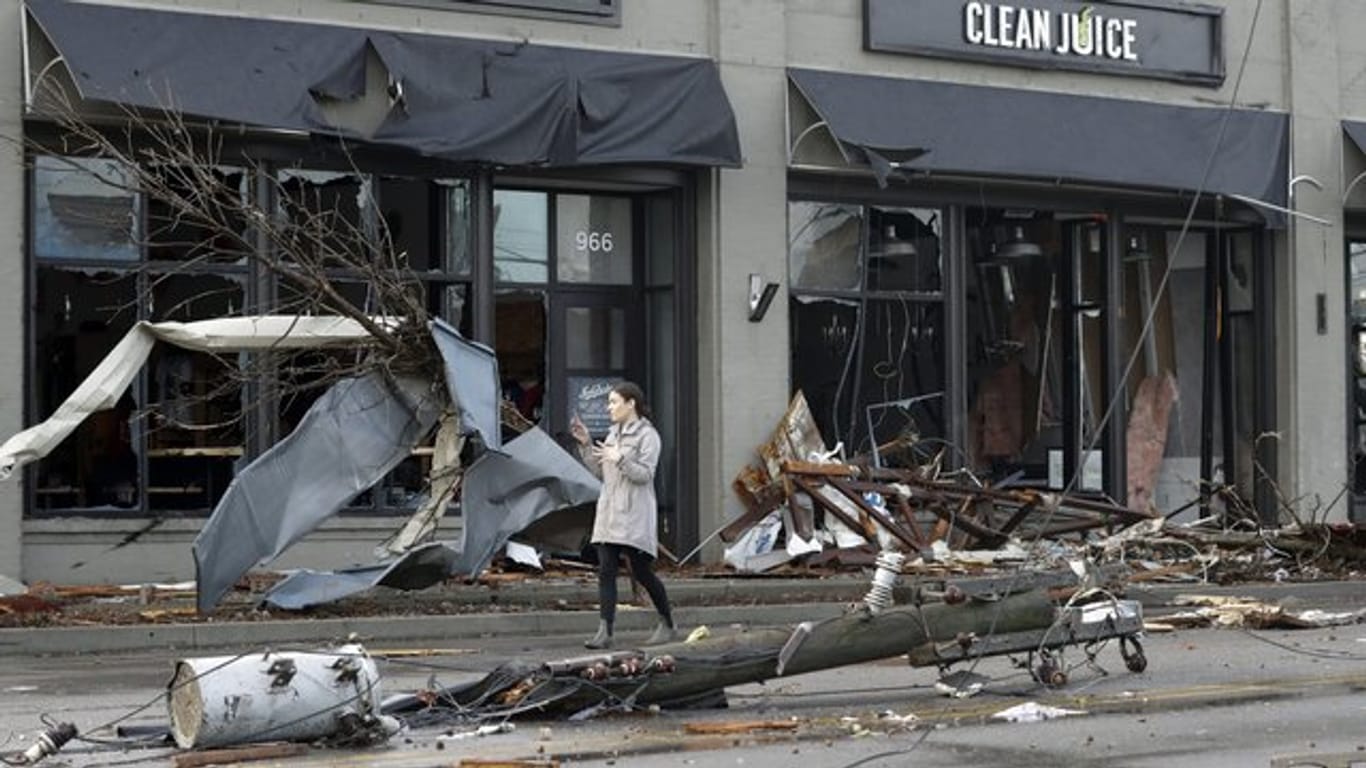 Eine Frau steht in Nashville vor einer zerstörten Fassade; auf der Straße liegt ein zerstörter Strommast.