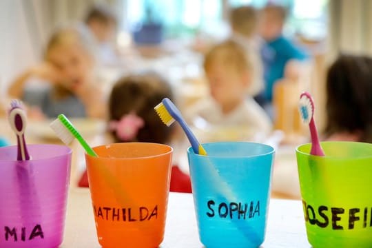 Zahnbürsten und Zahnputzbecher mit den Vornamen der Kinder stehen in einer Kindertagesstätte auf einem Tisch.