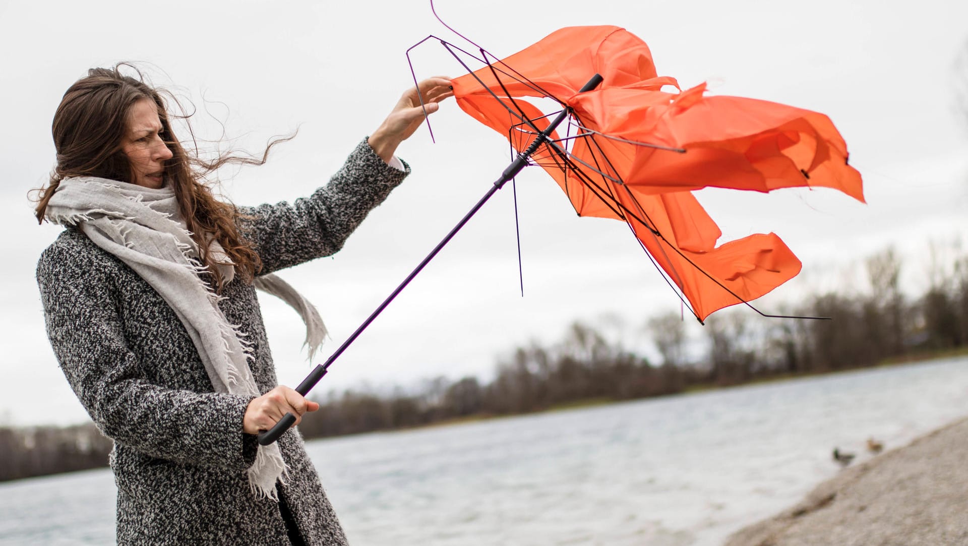 Eine Frau hält einen kaputten Regenschirm: In der nächsten Woche wird es wieder stürmisch. Eine Frau hält einen kaputten Regenschirm: In der nächsten Woche wird es wieder stürmisch.