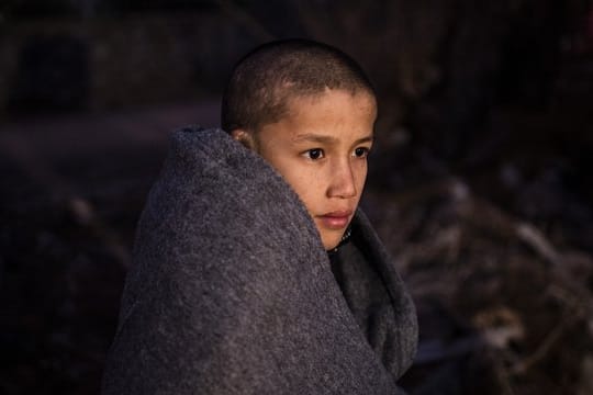 Ein Junge sitzt in Decken eingewickelt am Strand des Dorfes Skala Sikamias, nachdem er mit einem Beiboot die Ägäis von der Türkei aus überquert hat.