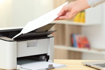 Eine Frau nimmt ein Blatt aus einem Drucker: Nach Windows-Updates kann es zu Druckerproblemen kommen.
