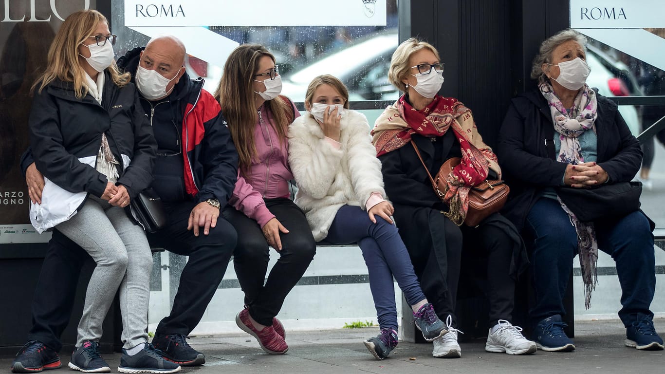 Reisende mit Mundschutzmasken warten in Italien an einer Bushaltestelle: Das ganze Land ist jetzt eine Sperrzone.