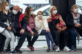 Reisende mit Mundschutzmasken warten in Italien an einer Bushaltestelle: Das ganze Land ist jetzt eine Sperrzone.
