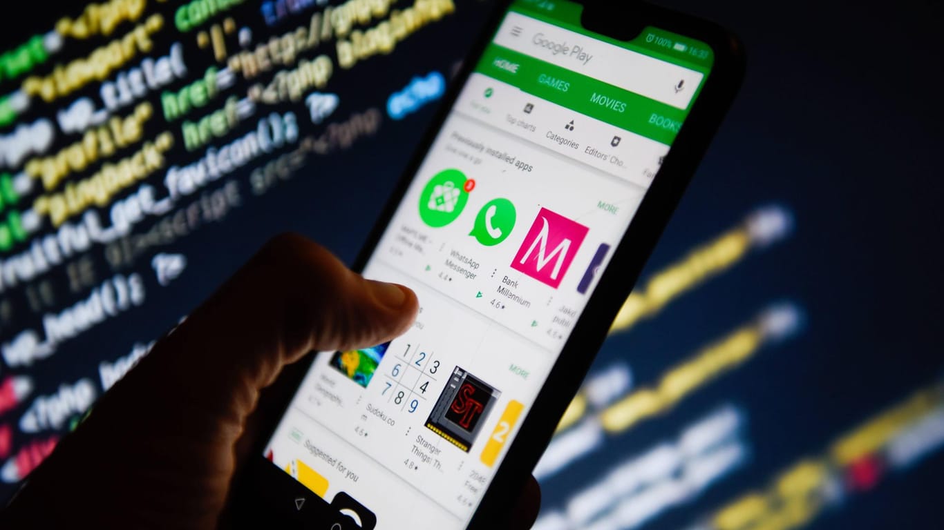 Google Play Store ist auf einem Smartphone geöffnet. Im Hintergrund sieht man Code-Zeilen: Manche Apps sollen heimlich Nutzerdaten sammeln.