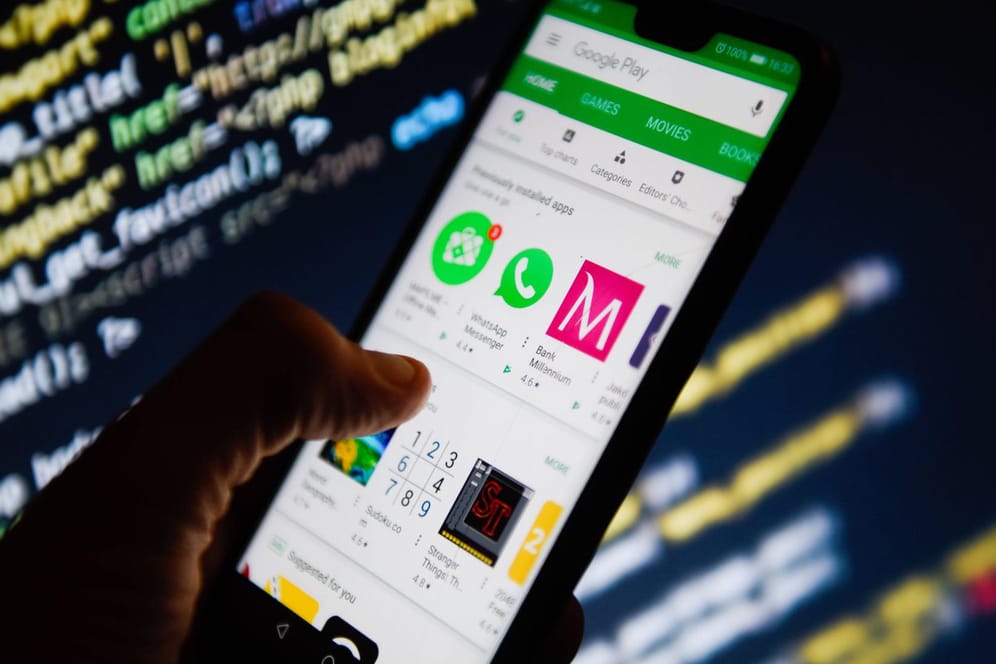 Google Play Store ist auf einem Smartphone geöffnet. Im Hintergrund sieht man Code-Zeilen: Manche Apps sollen heimlich Nutzerdaten sammeln.