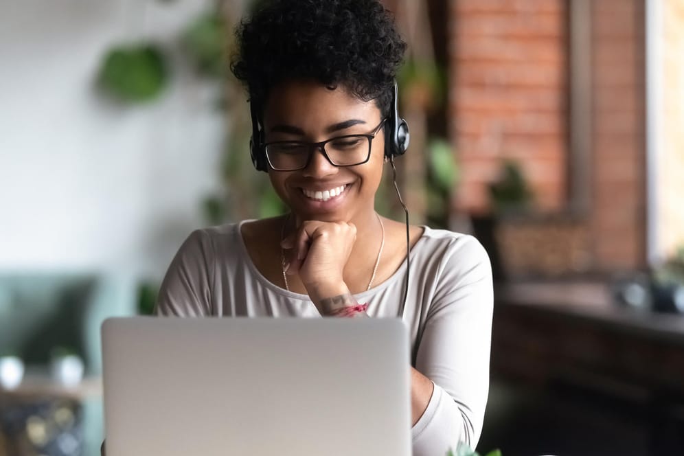 Eine junge Frau schaut auf ihren Laptop: Mit einem ETF-Sparplan investieren Sie regelmäßig eine bestimmte Summe in einen Indexfonds – ganz leicht von zu Hause im Internet.