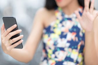 Eine junge Frau winkt in die Smartphone-Kamera: Mit einem Trick lassen sich Videoanrufe auf dem iPhone aufzeichnen.