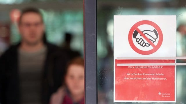 "Aus Aktuellem Anlass: Wir schenken Ihnen einen Lächeln, aber verzichten auf den Händedruck" steht auf einer Glastür einer Sparkasse. "Aus Aktuellem Anlass: Wir schenken Ihnen einen Lächeln, aber verzichten auf den Händedruck" steht auf einer Glastür einer Sparkasse.