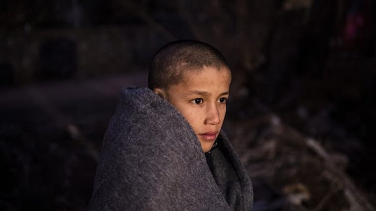 Ein Junge sitzt in Decken eingewickelt in der Nähe eines Dorfes auf Lesbos.