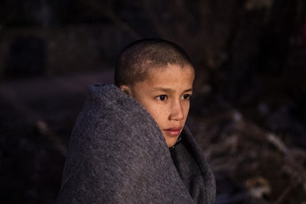 Ein Junge sitzt in Decken eingewickelt in der Nähe eines Dorfes auf Lesbos.