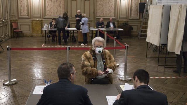 Eine Wählerin mit Atemschutzmaske registriert sich in einem Wahllokal in der französisch-italienischen Grenzstadt Menton. Eine Wählerin mit Atemschutzmaske registriert sich in einem Wahllokal in der französisch-italienischen Grenzstadt Menton.