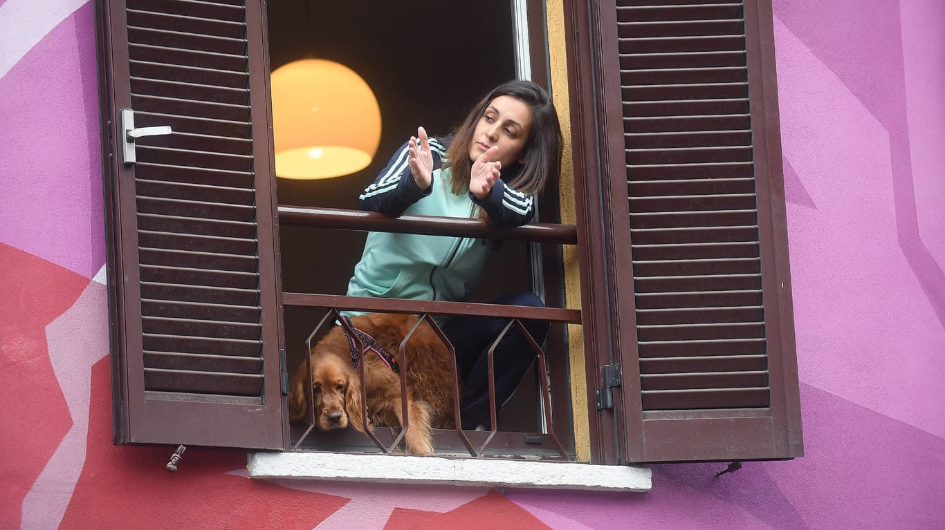 Sperrzone in Italien: Eine Frau applaudiert am Fenster ihrer Wohnung in der Innenstadt von Mailand vorbeifahrenden Einsatzfahrzeugen, Ärzten und Sanitätern.