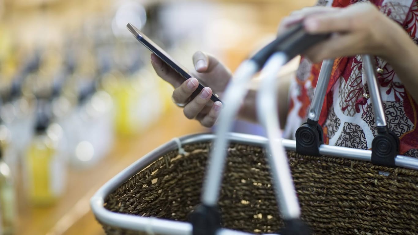Eine Frau hält einen Einkaufskorb und ihr Smartphone (Symbolbild): In Mainz bieten Freiwillige an, für Risikogruppen einkaufen zu gehen.