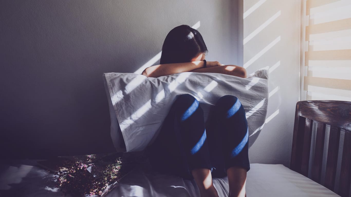 Eine Frau sitzt in der Hocke auf einem Bett: Depressiven Menschen fällt es oft schwer, am sozialen Leben teilzunehmen.