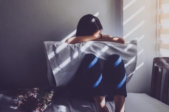 Eine Frau sitzt in der Hocke auf einem Bett: Depressiven Menschen fällt es oft schwer, am sozialen Leben teilzunehmen.