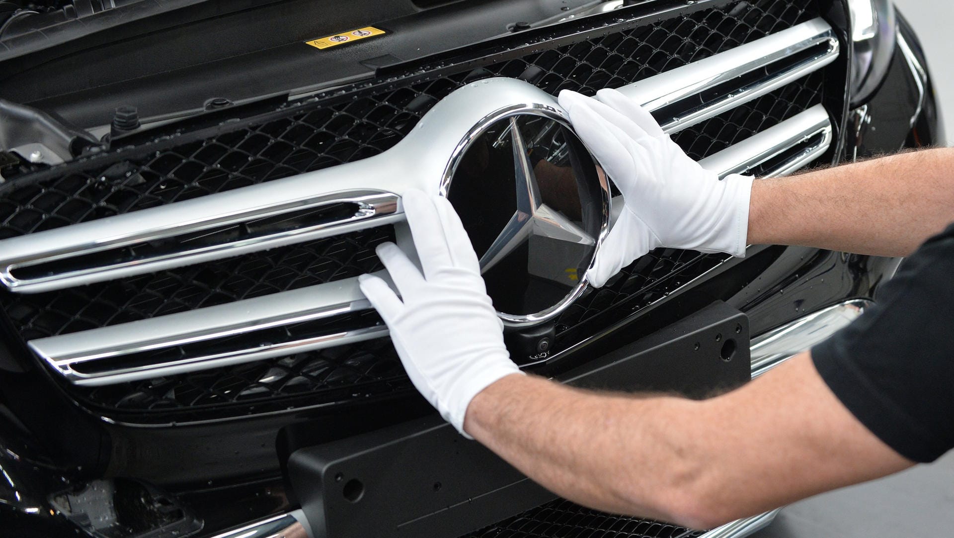 Ein Daimler-Werksmitarbeiter passt die Kühlerhaube eines Mercedes an: Der Autobauer fährt seine Produktion wegen der Corona-Krise herunter.