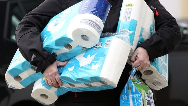 Ein Mann trägt Toilettenpapier und Küchenrollen aus einem Supermarkt.
