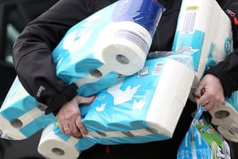 Ein Mann trägt Toilettenpapier und Küchenrollen aus einem Supermarkt.