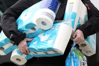 Ein Mann trägt Toilettenpapier und Küchenrollen aus einem Supermarkt.