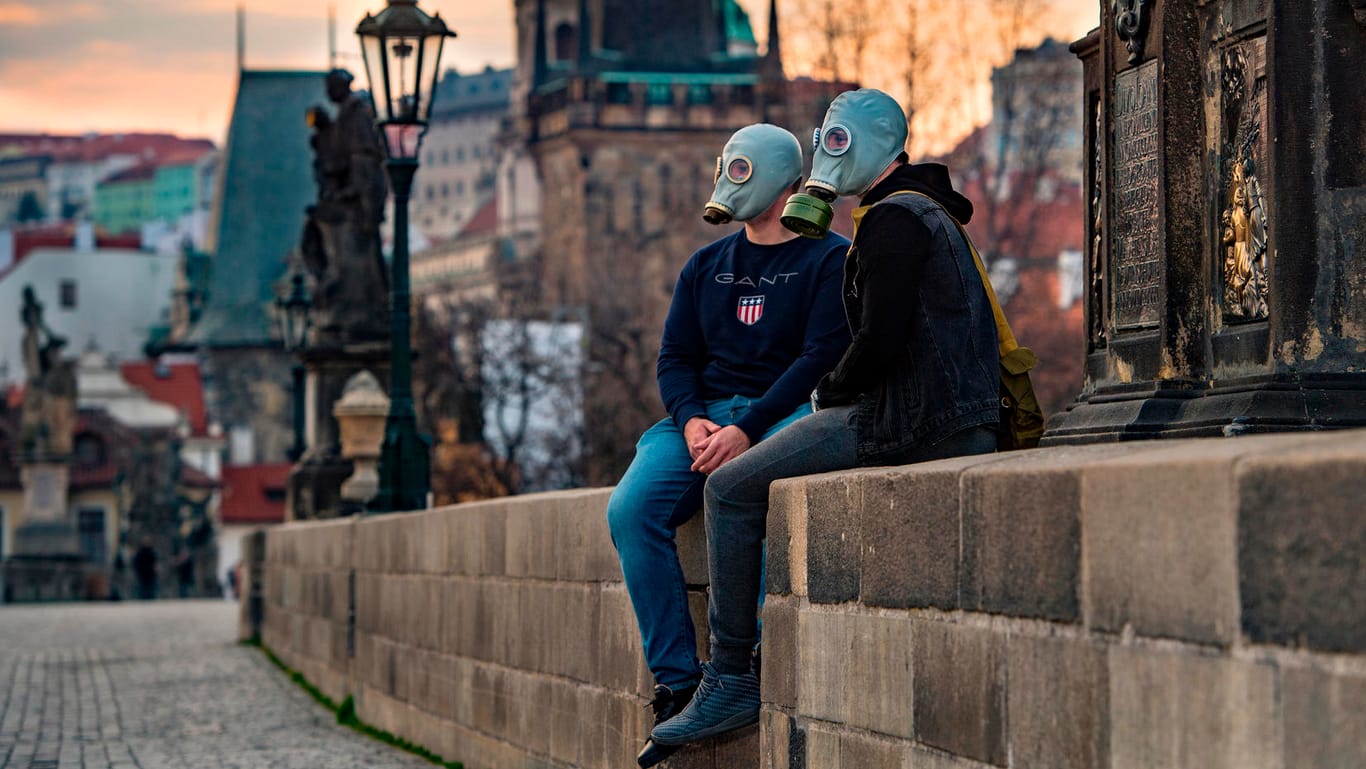 Ein Paar mit Gasmasken sitzt auf der Karlsbrücke in Prag: Die tschechische Regierung hat striktere Maßnahmen gegen das Coronavirus eingeführt als Deutschland.