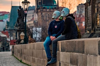Ein Paar mit Gasmasken sitzt auf der Karlsbrücke in Prag: Die tschechische Regierung hat striktere Maßnahmen gegen das Coronavirus eingeführt als Deutschland.