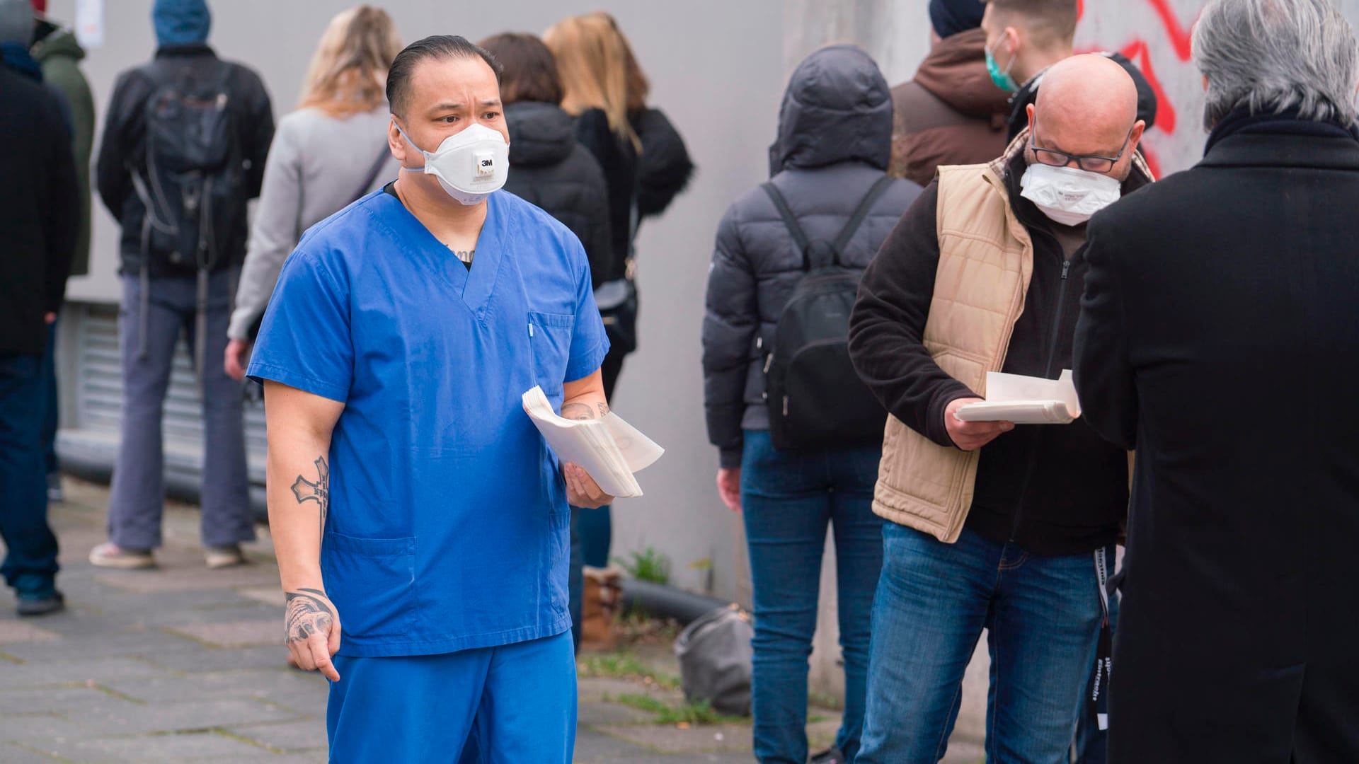 Coranavirus-Tests: Mitarbeiter verteilen Wartenummern an Menschen auf dem Gehweg am Corona-Testcenter des Ärztlichen Bereitschaftsdienstes Hessen.