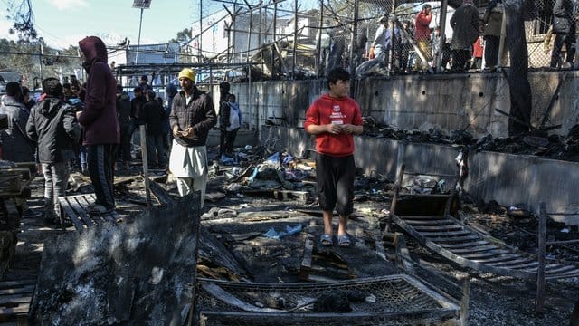 Migranten stehen auf den abgebrannten Überresten des Gemeinschaftszentrums. Migranten stehen auf den abgebrannten Überresten des Gemeinschaftszentrums.