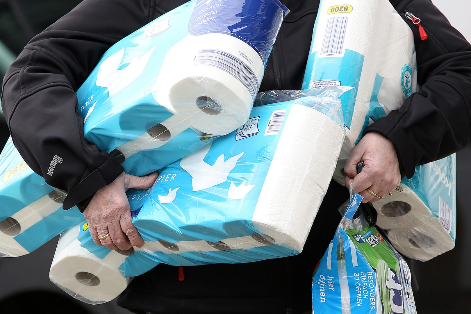 Jemand trägt mehrere Packungen Toilettenpapier: Auf Ebay Kleinanzeigen häufen sich die Wucherangebote.