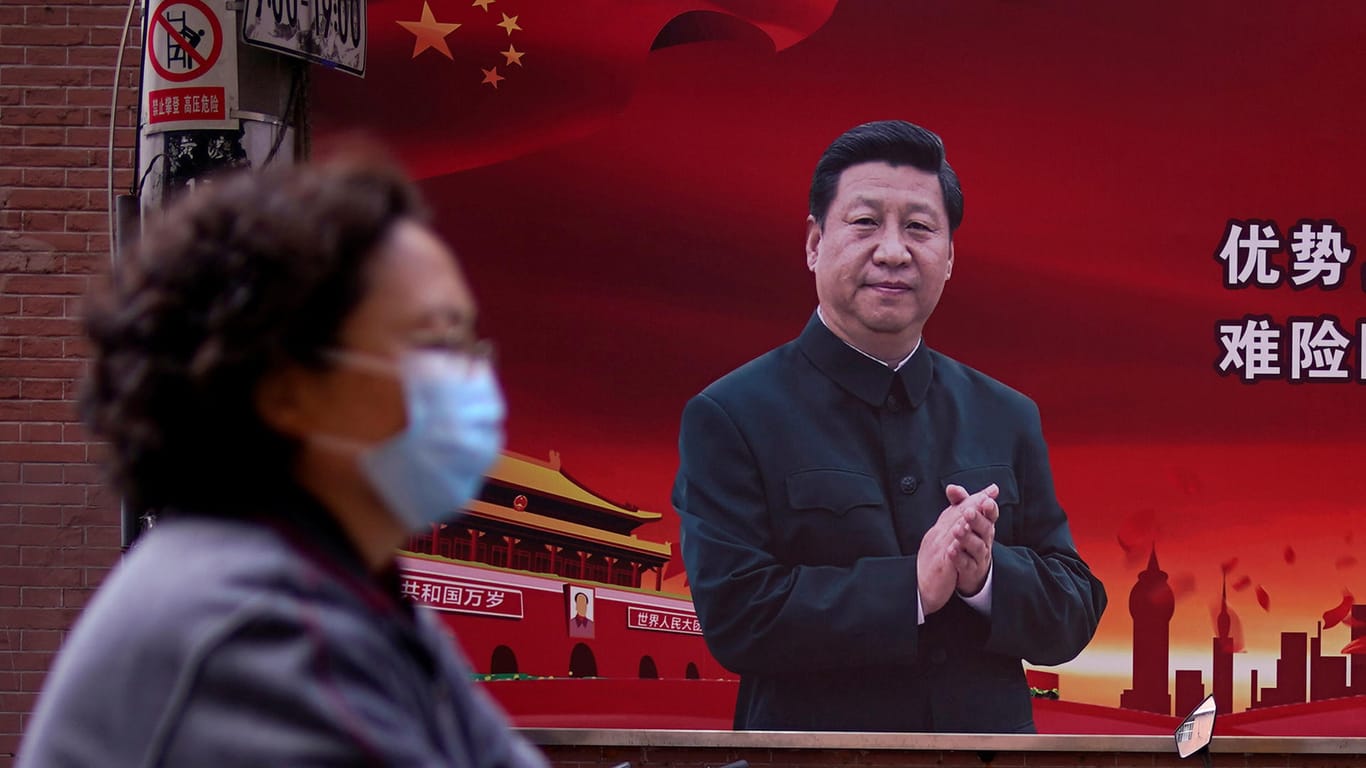 Frau mit Atemmaske vor einem Porträt des chinesischen Staatspräsidenten Xi Jinping: Kritik an der Corona-Strategie der staatlichen Führung führt rasch zur Einstufung als Dissident.