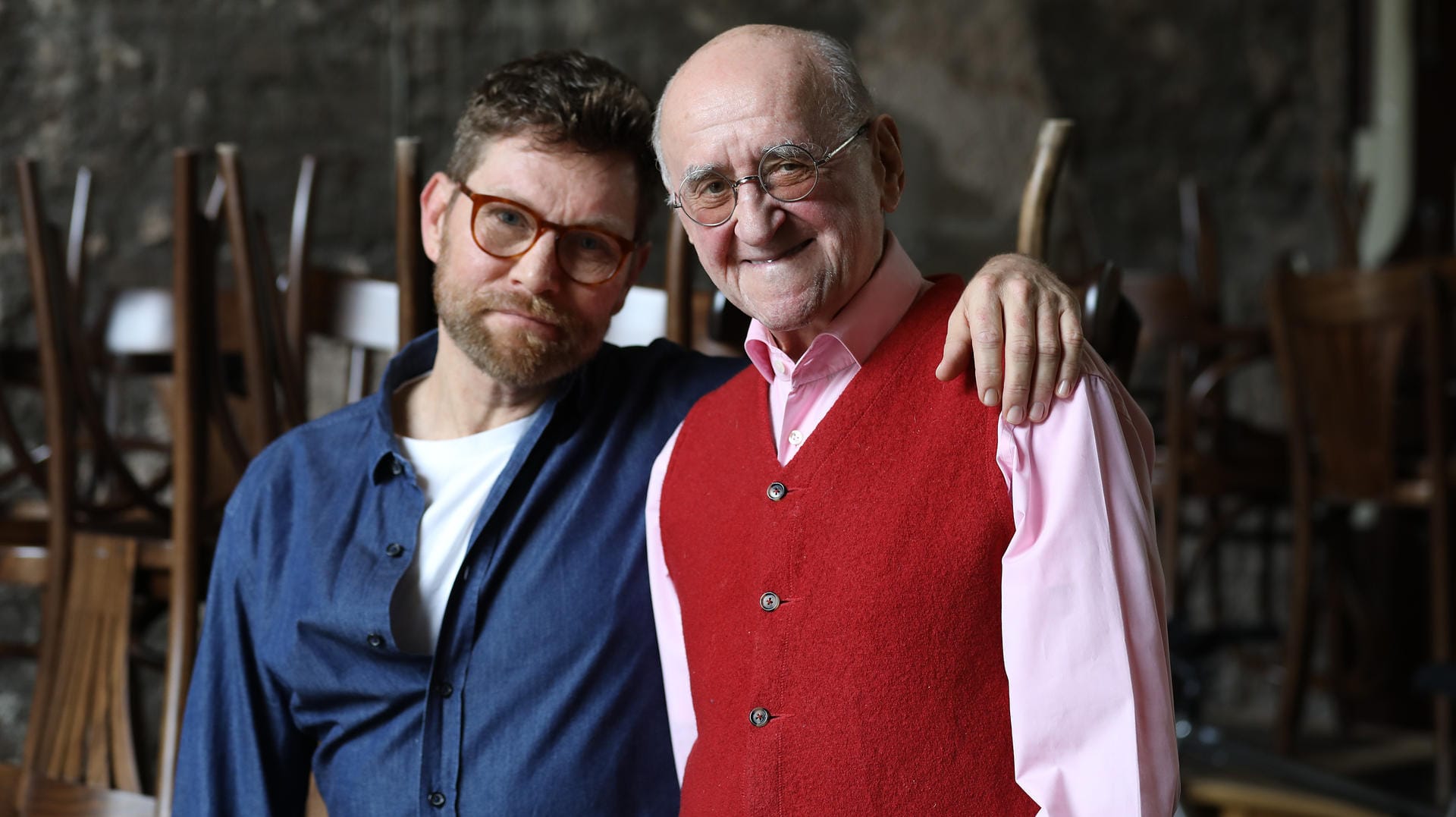 Scott Biolek-Ritchie (links), Adoptivsohn von Alfred Biolek, und Alfred Biolek stehen zusammen in einem Restaurant.