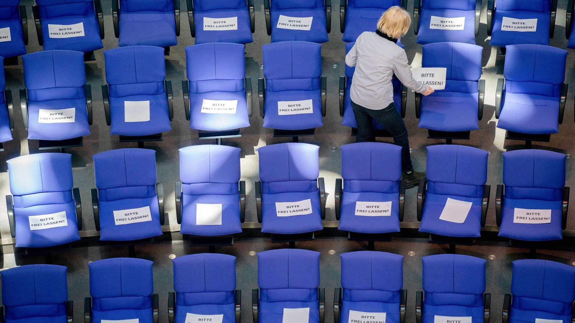 Mitarbeiter des Bundestags legen Zettel mit der Aufschrift "Bitte frei lassen" auf die Stühle der Abgeordneten im Plenarsaal. Damit müssen die Bundestagsabgeordneten bei der kommenden Sitzung am Mittwoch immer zwei Plätze unbesetzt lassen, um die Abstandsregel gegen die Verbreitung des Coronavirus einzuhalten.
