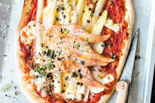 Auf den fertigen Pizzateig kommen Tomatensugo, Parmesan, Mozzarella, Lachs, Spargel, Kapern und Zitronenthymian.