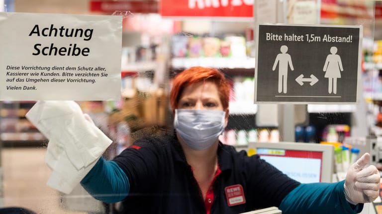 Eine Mitarbeiterin in einem Supermarkt putzt eine Plexiglasscheibe, einen sogenannten "Spuckschutz" (Symbolbild): Um die Ausbreitung des Coronavirus zu verlangsamen, hat die Bundesregierung das öffentliche Leben weiter erheblich eingeschränkt.
