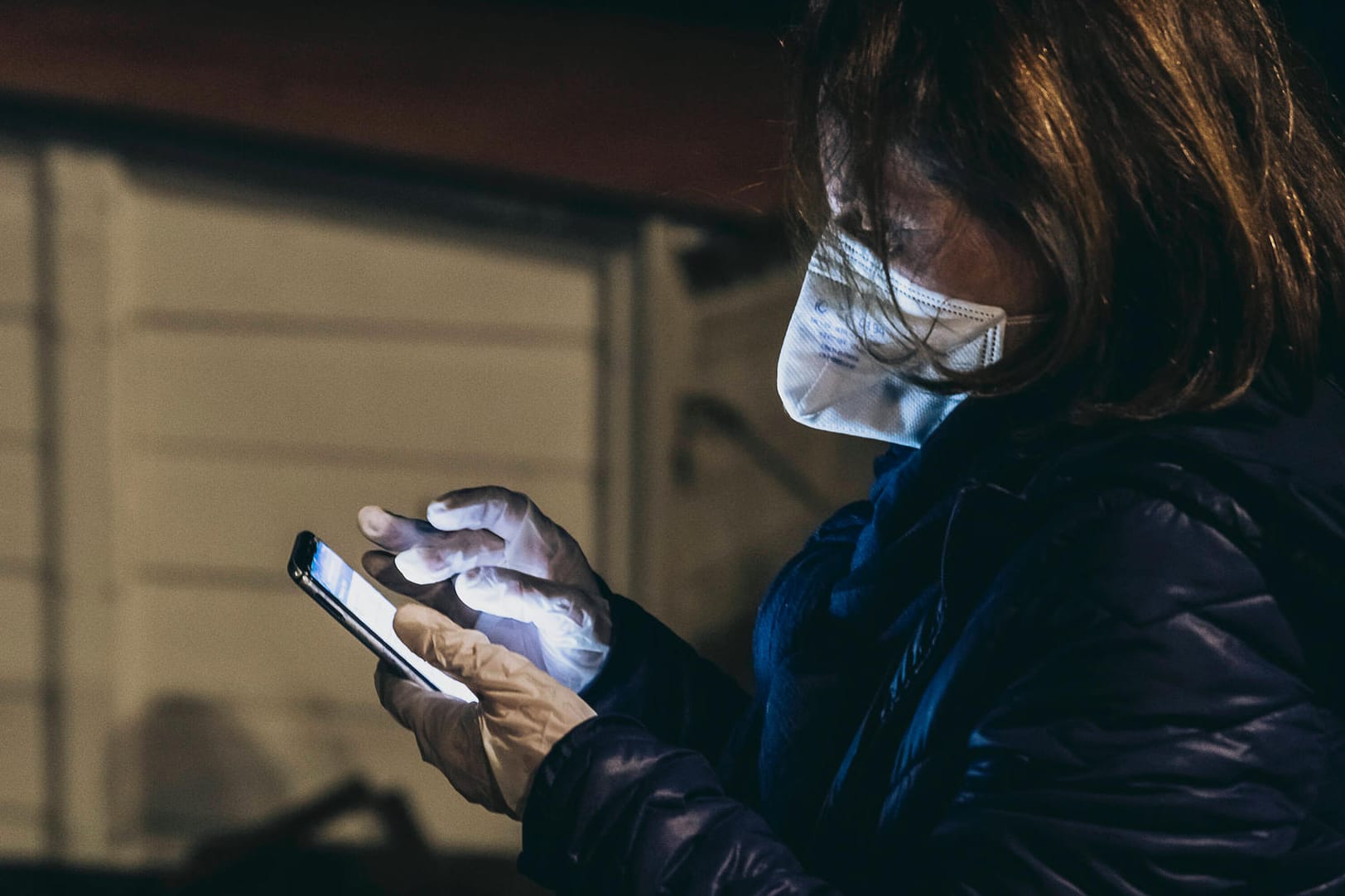 Eine Frau mit Atemschutzmaske und Handschuhen tippt in ein Smartphone: Bürger in Hagen können die Corona-Hotline nun noch länger erreichen (Symbolbild).