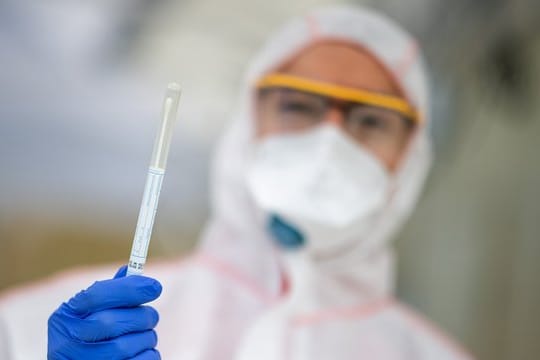 Ein Mitarbeiter hält in einem Corona-Abstrichzentrum einen Abstrich in der Hand.