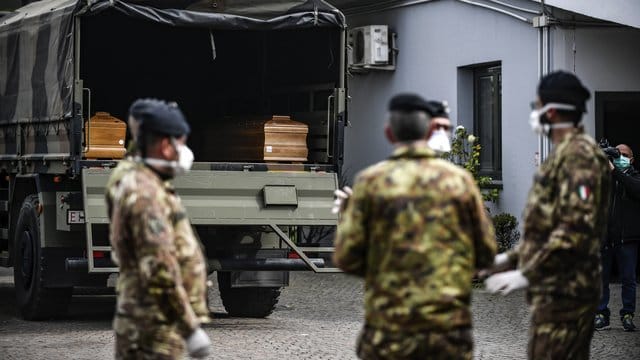 Italienische Soldaten mit Mundschutz vor einem Militärfahrzeug mit Särgen von Corona-Opfern. Italienische Soldaten mit Mundschutz vor einem Militärfahrzeug mit Särgen von Corona-Opfern.