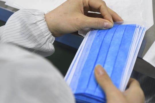 Ein Mitarbeiter eines Herstellers medizinischer Geräte verpackt in einer Produktionswerkstatt Mundschutz-Masken.