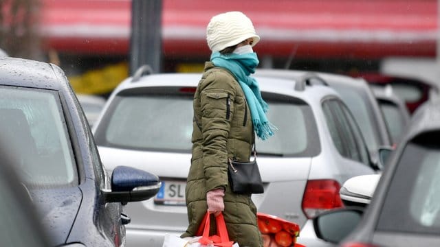 Eine Frau mit Mundschutz trägt ihre Einkäufe über den Parkplatz eines Einkaufszentrums in Salzburg. Eine Frau mit Mundschutz trägt ihre Einkäufe über den Parkplatz eines Einkaufszentrums in Salzburg.