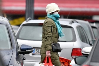 Eine Frau mit Mundschutz trägt ihre Einkäufe über den Parkplatz eines Einkaufszentrums in Salzburg.