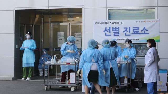 Medizinisches Personal in Schutzausrüstung steht vor einem Krankenhaus in Südkorea.