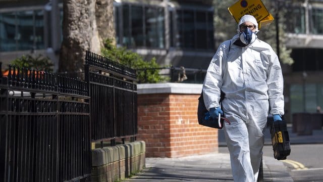 Ein Mann geht im Schutzanzug über eine Straße in Westminster im Zentrum Londons. Ein Mann geht im Schutzanzug über eine Straße in Westminster im Zentrum Londons.
