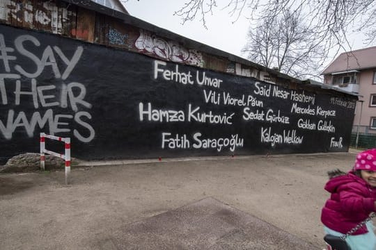 Ein kleines Mädchen schaukelt vor der Wand eines Jugendzentrums, auf dem die Namen der Opfer des Anschlags vom 19.