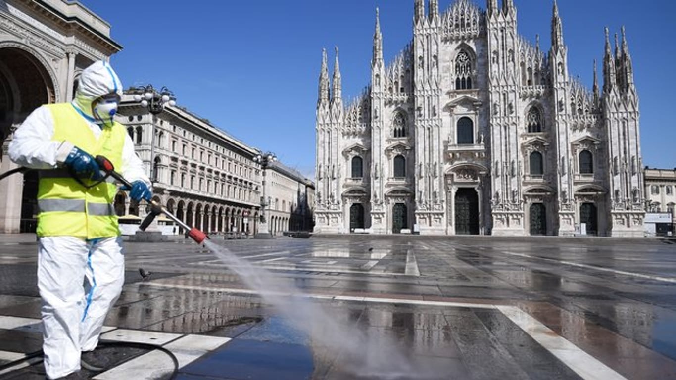 Ein Arbeiter in Schutzanzug reinigt den Boden auf der Piazza del Duomo in Mailand.