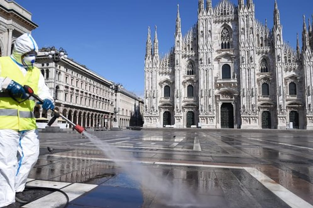 Ein Arbeiter in Schutzanzug reinigt den Boden auf der Piazza del Duomo in Mailand.