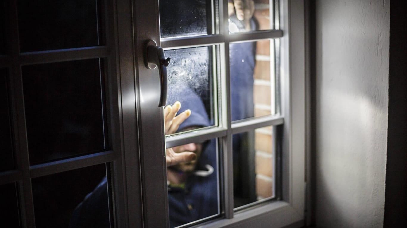 Ein Mann steht mit einer Taschenlampe vor einem Fenster (Symbolbild): In Bielefeld konnte eine Frau einen Einbrecher in die Flucht schlagen.
