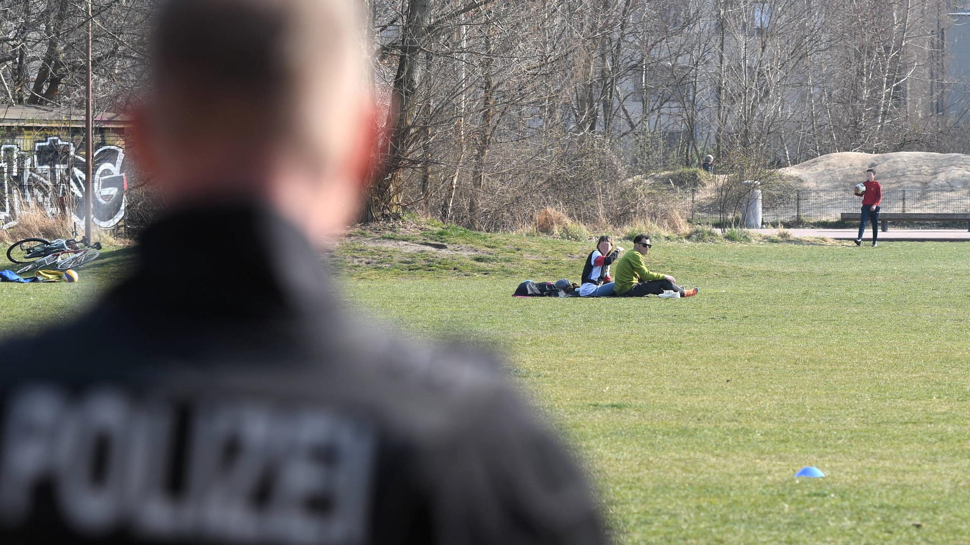 Polizist blickt auf Wiese im Park am Gleisdreieck: Berliner Polizisten kontrollieren die Einhaltung der Corona-Maßnahmen.